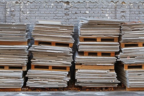 Asbestos cement sheets on pallets on the background of a brick fence